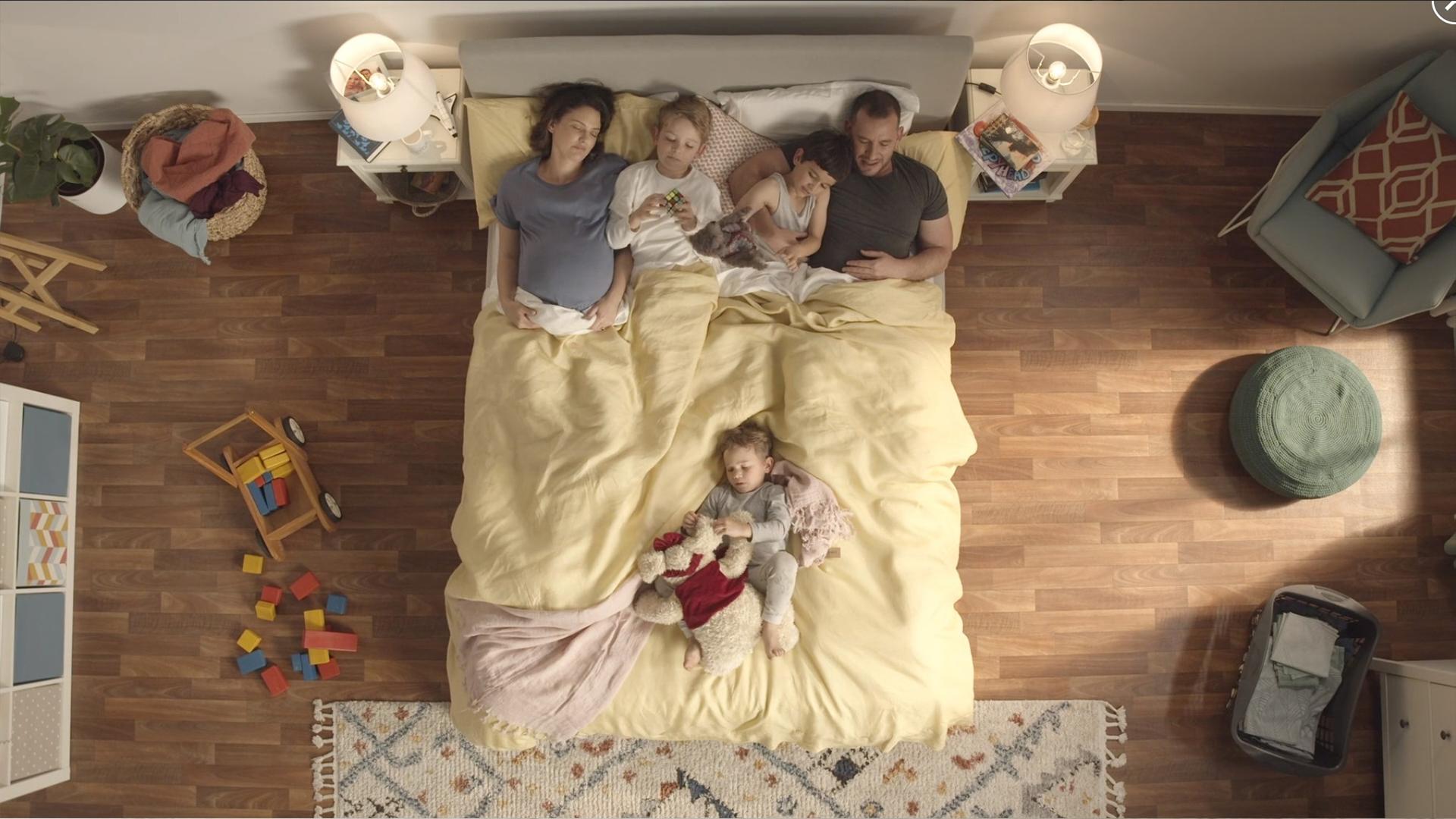 A pregnant woman and a man sleeping in a SD Mach 2 bed with their three kids, one sleeping near the foot of the bed spread out. 