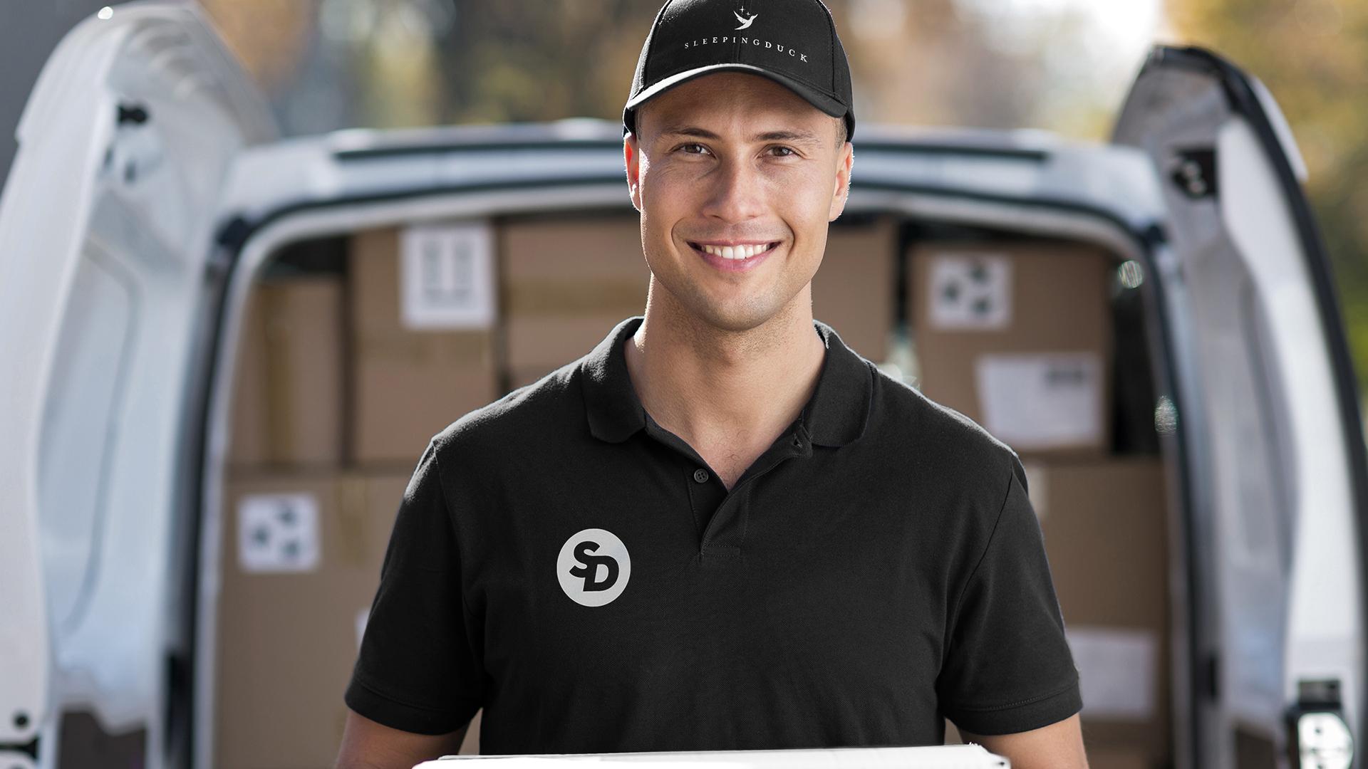 Delivery man in a Sleeping Duck uniform smiling in front of a full delivery van.