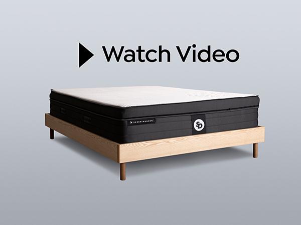 The words "Watch Video" floating above a Sleeping Duck Mattress on an SD Indestruct Baker Bed Base.